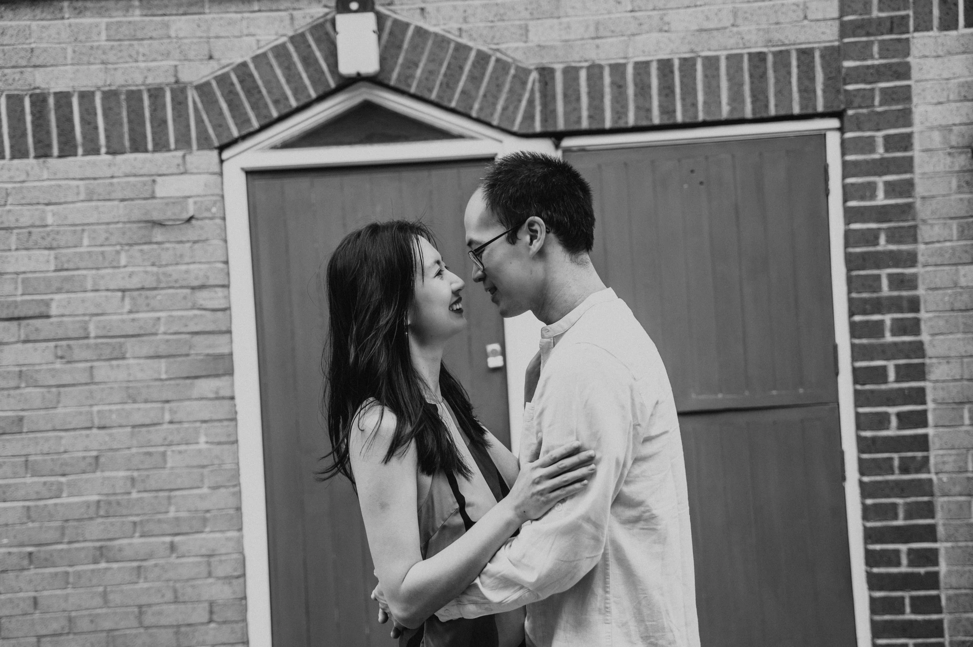 A black-and-white close portrait of the couple leaning towards each other in front of a garage door during their London couple photoshoot.