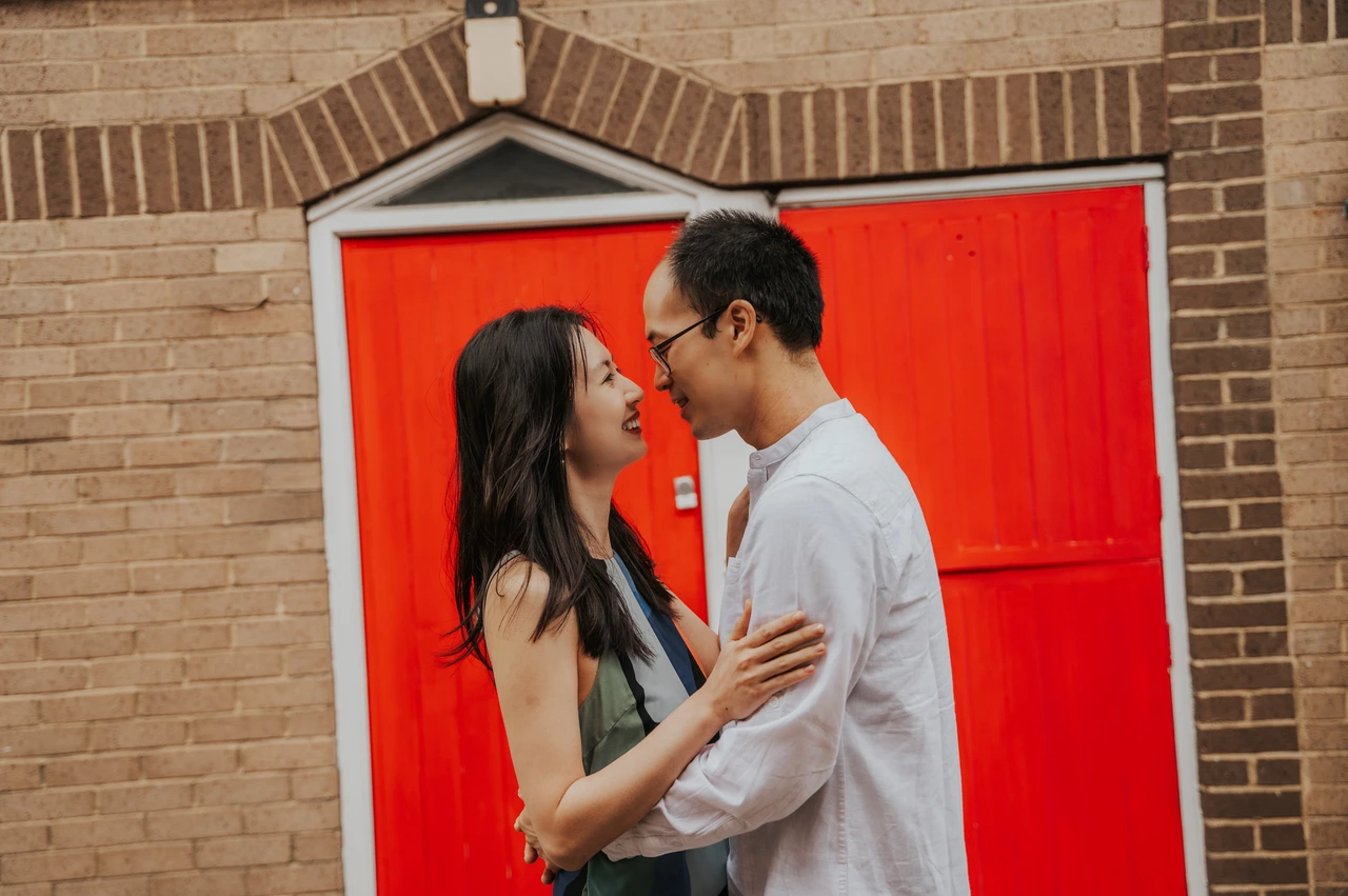 London couple photoshoot: leaning close beside a red garage door A close portrait of the couple leaning towards each other beside a vivid red garage door in Notting Hill during their London couple photoshoot.