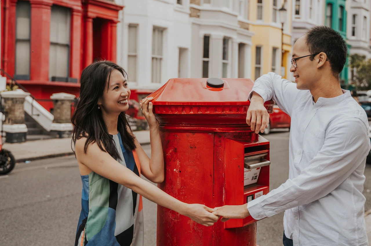 London couple photoshoot: holding hands across a red postbox A close landscape portrait of the couple holding hands across a red postbox and looking at each other during their London couple photoshoot.