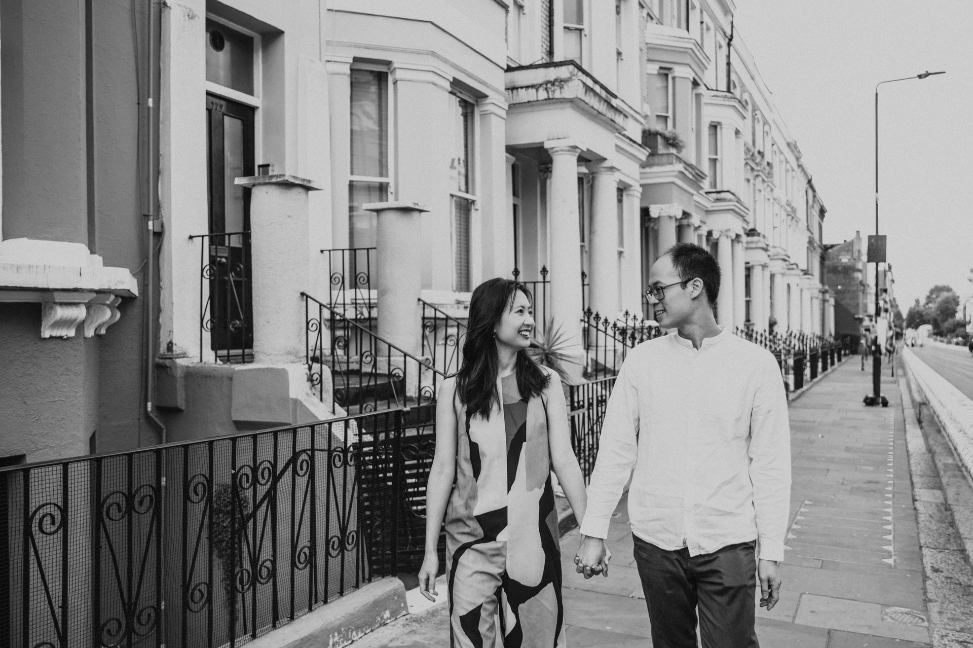 A black-and-white view of the couple walking together beside the railings and terraced houses of Notting Hill during their London couple photoshoot.
