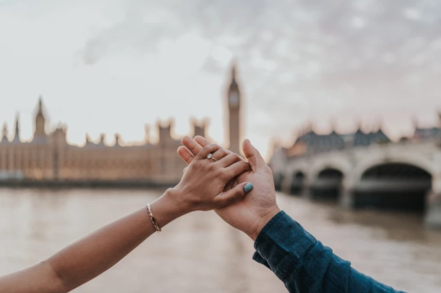 Close-up of the couple’s raised joined hands with Big Ben and Westminster Bridge softly blurred behind, from their London couple photoshoot.