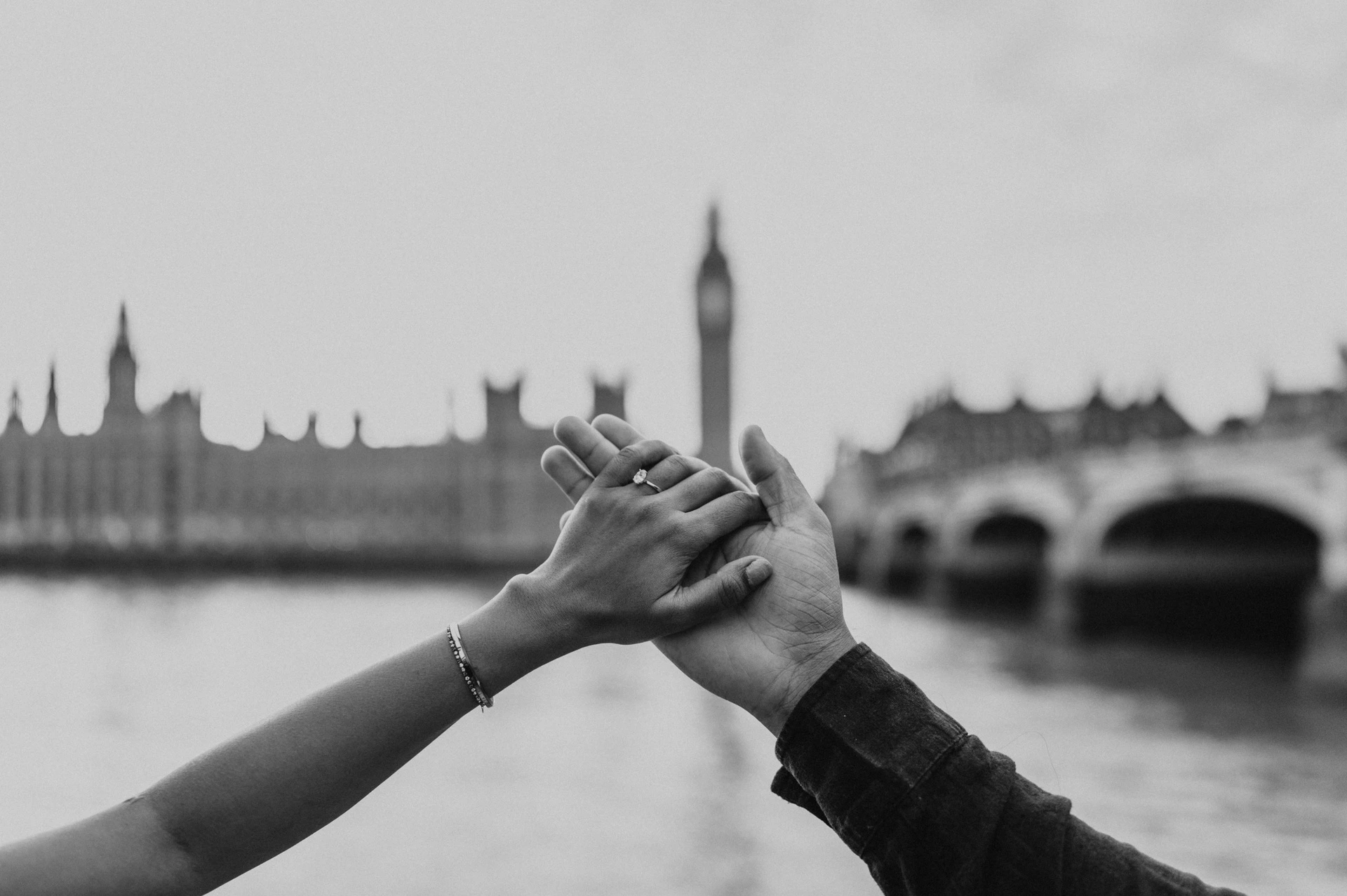 Black-and-white close-up of the couple’s raised joined hands, with Big Ben and Westminster Bridge blurred behind, from their London couple photoshoot.