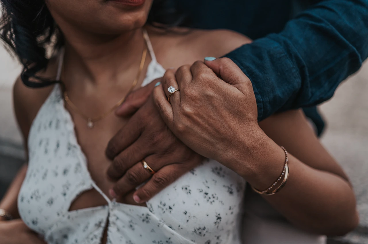 London couple photoshoot with a close view of their hands Close-up of the woman holding her partner’s hand across her shoulder, showing their rings and her floral dress, during their London couple photoshoot.