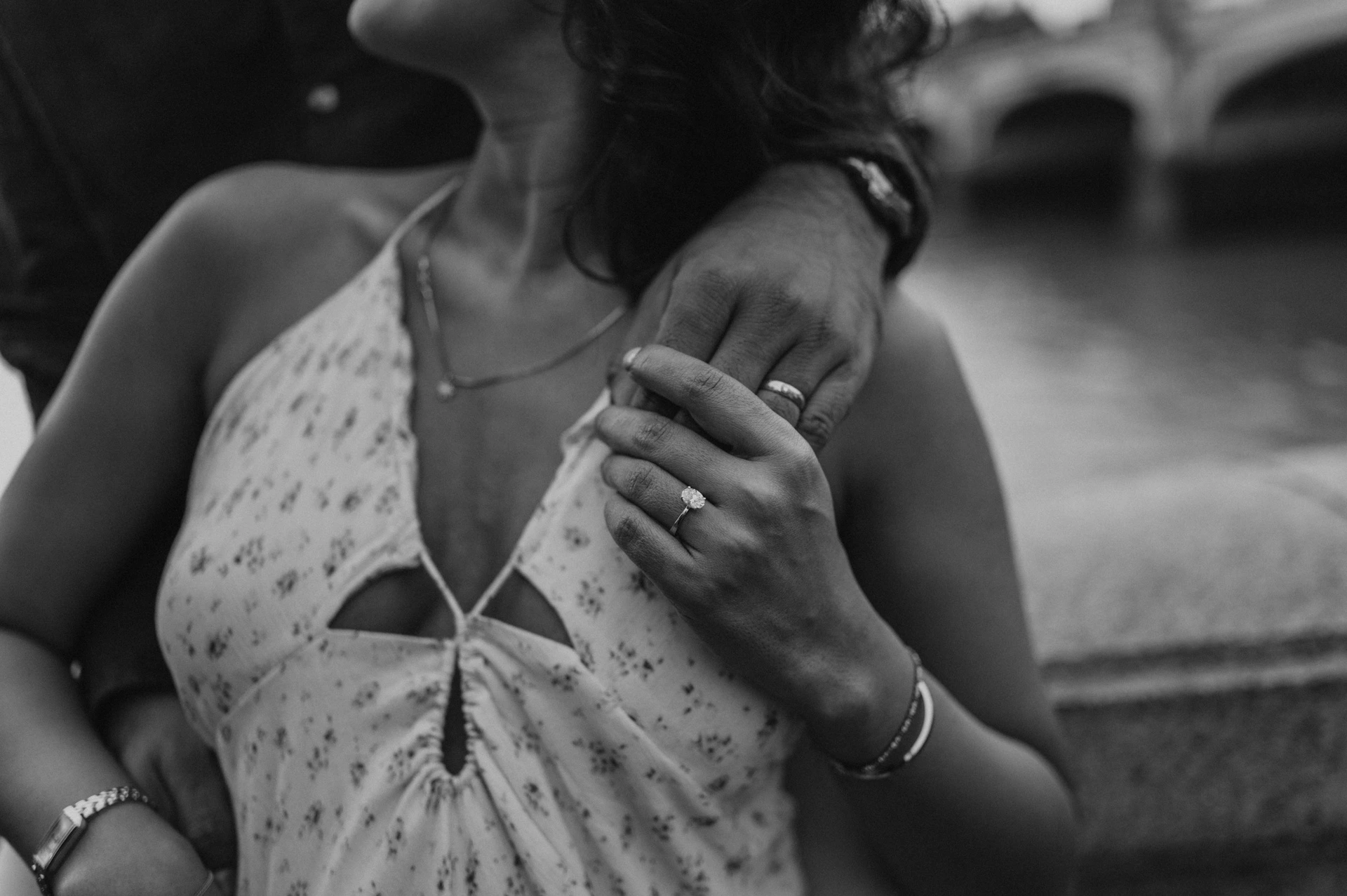 Black-and-white close-up of the couple’s hands at the woman’s shoulder and the neckline of her floral dress, from their London couple photoshoot.