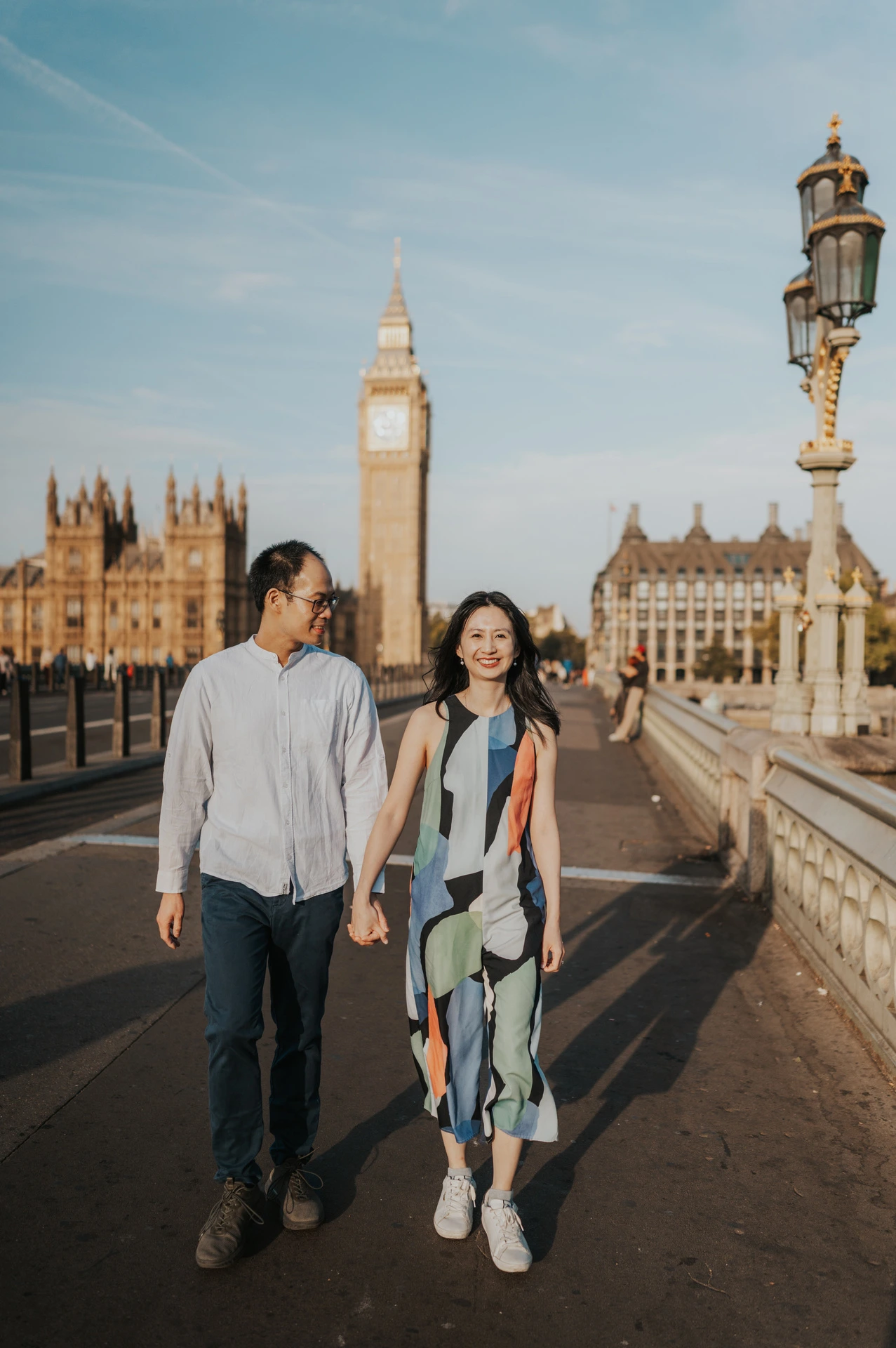Couple walking together on Westminster Bridge, with an ornate lamp and Big Ben behind them, during their London couple photoshoot.