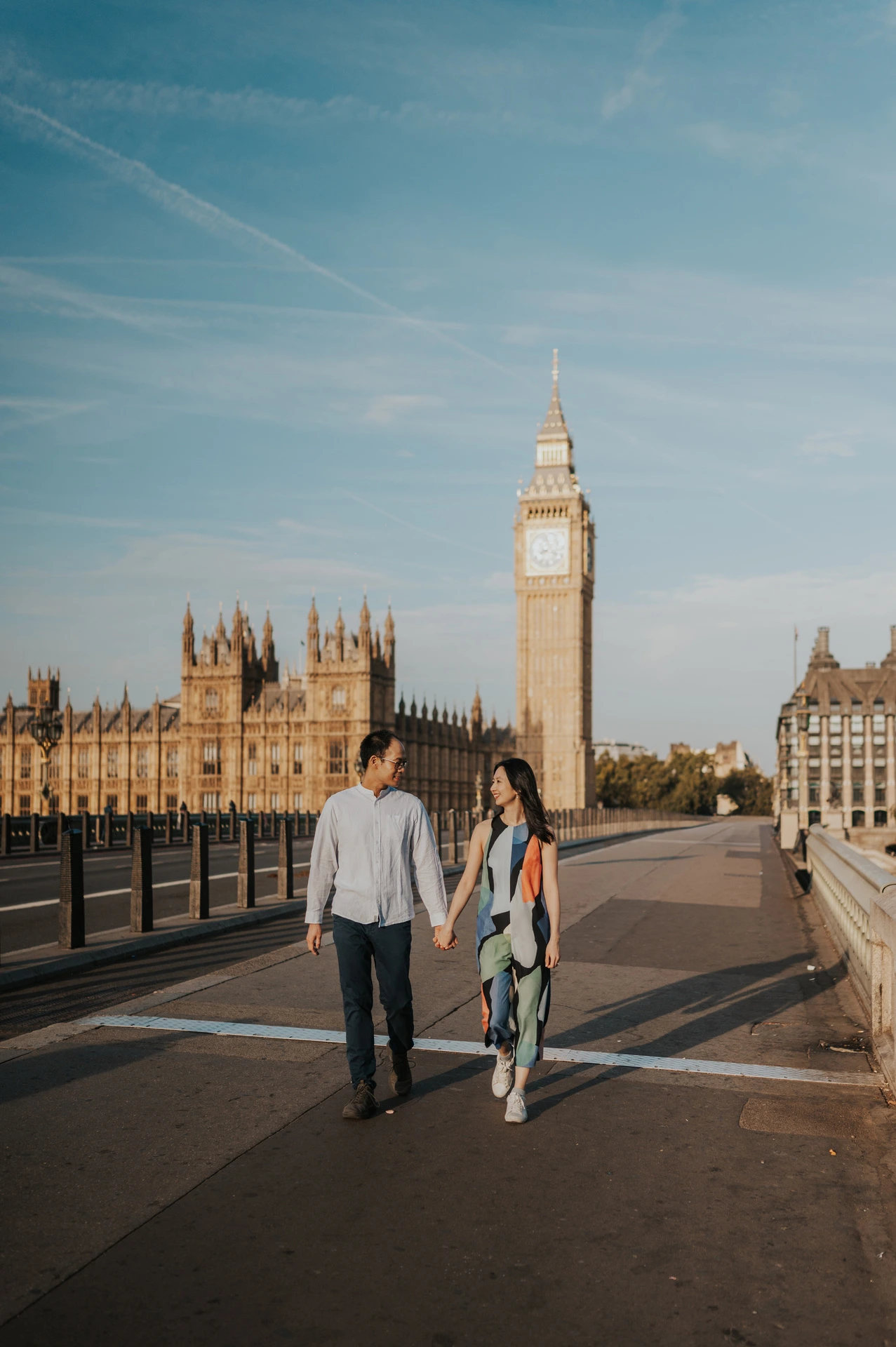 Wide full-length view of the couple walking along Westminster Bridge with Big Ben behind them during their London couple photoshoot.