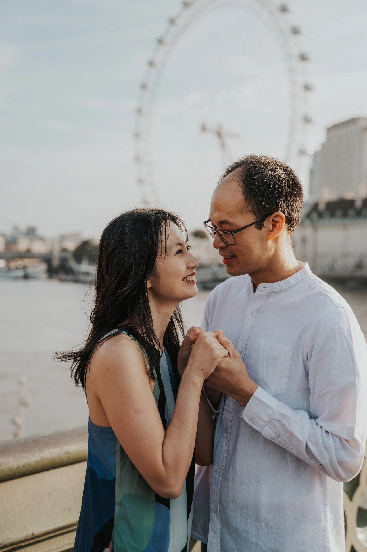 Close portrait of the couple smiling at each other beside the Thames, with the London Eye behind them, during their London couple photoshoot.