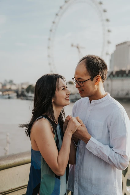 Close portrait of the couple smiling at each other beside the Thames, with the London Eye behind them, during their London couple photoshoot.