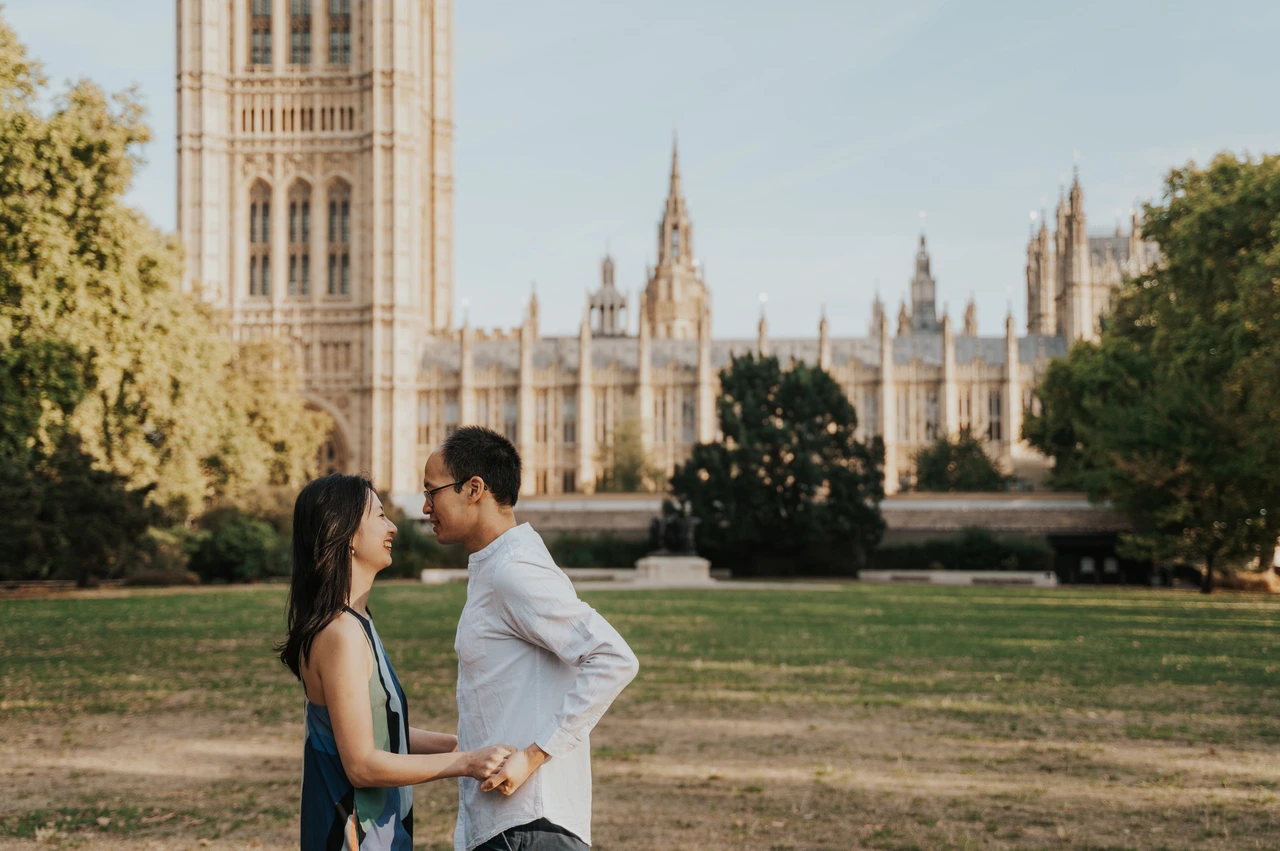 London couple photoshoot holding hands in the Westminster gardens Close landscape portrait of the couple holding hands in Victoria Tower Gardens, with Parliament in the background, during their London couple photoshoot.