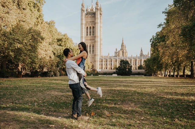 Wide landscape view of the couple sharing a lift on the lawn of Victoria Tower Gardens during their London couple photoshoot.