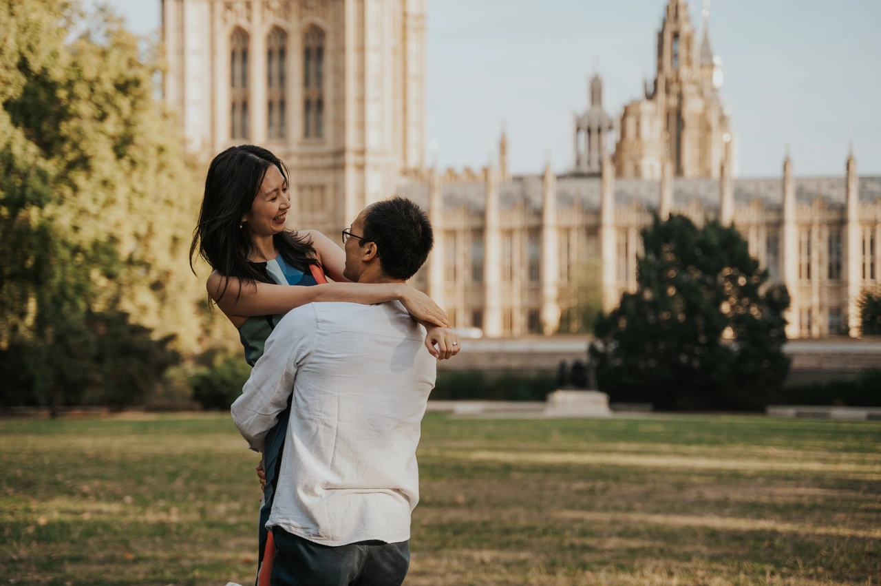 London couple photoshoot smiling during a lift by Parliament Close portrait of the couple smiling during a lift in Victoria Tower Gardens, with Parliament behind them, during their London couple photoshoot.