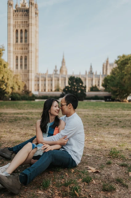 Couple sitting close together on the lawn beneath Victoria Tower, with the woman in a colourful dress, during their London couple photoshoot.