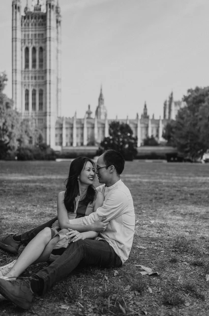 Black-and-white London couple photoshoot seated in the gardens Black-and-white portrait of the couple sitting closely together on the grass in Victoria Tower Gardens, from their London couple photoshoot.
