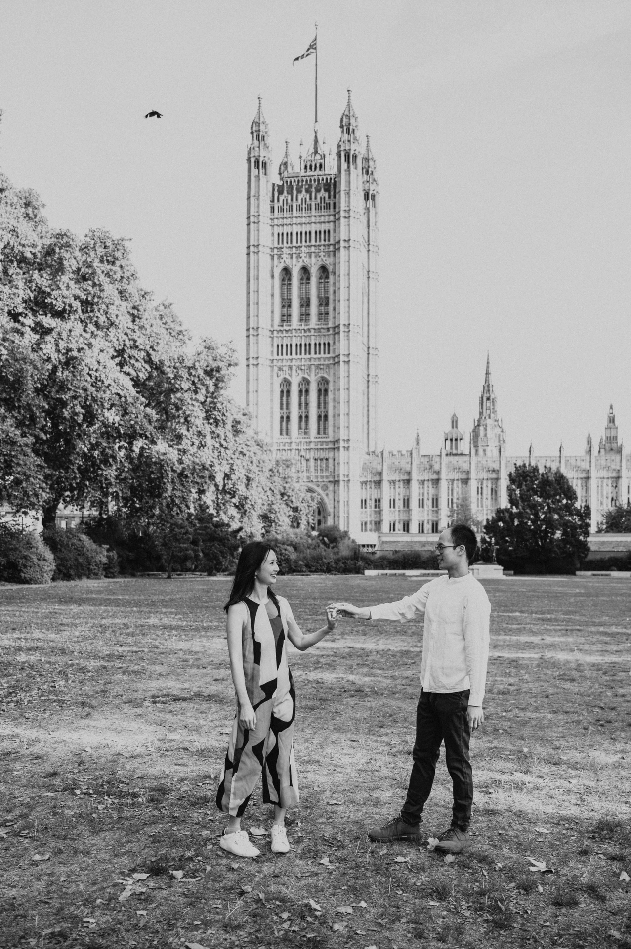 Black-and-white full-length portrait of the couple turning together on the lawn of Victoria Tower Gardens during their London couple photoshoot.