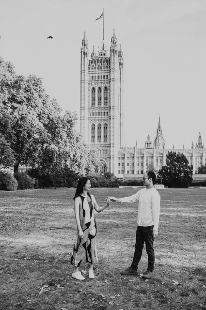 Black-and-white London couple photoshoot turning in the gardens Black-and-white full-length portrait of the couple turning together on the lawn of Victoria Tower Gardens during their London couple photoshoot.