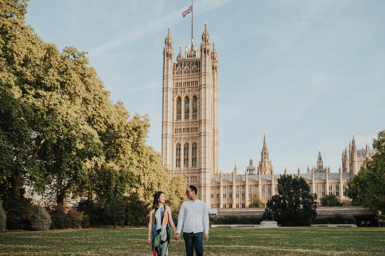 London couple photoshoot in Victoria Tower Gardens Couple holding hands on the lawn of Victoria Tower Gardens, with Parliament’s Victoria Tower behind them, during their London couple photoshoot.