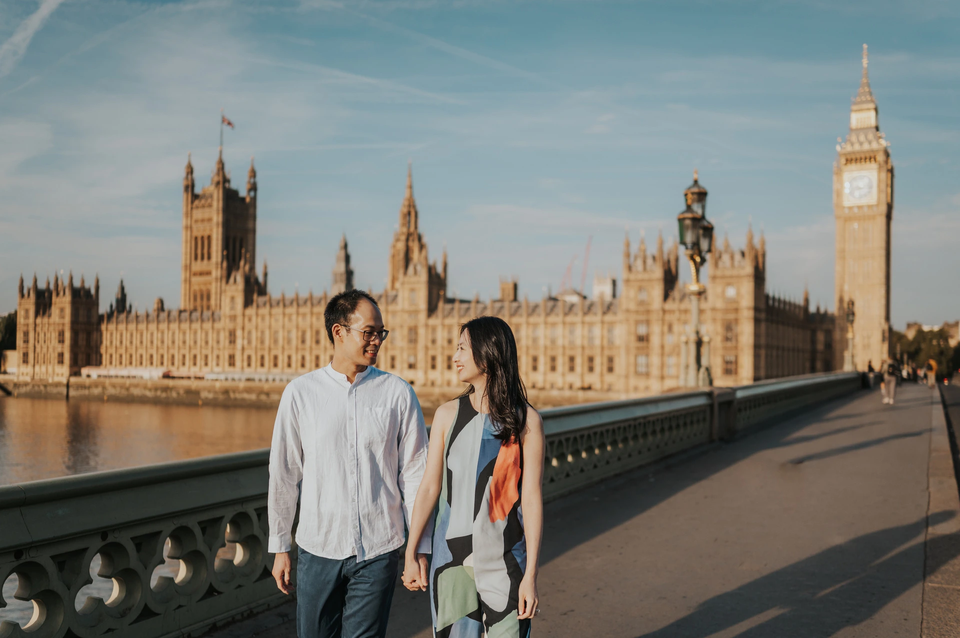 London couple photoshoot with Parliament and Big Ben Wide portrait of the couple holding hands on Westminster Bridge, with Parliament and Big Ben behind them, during their London couple photoshoot.