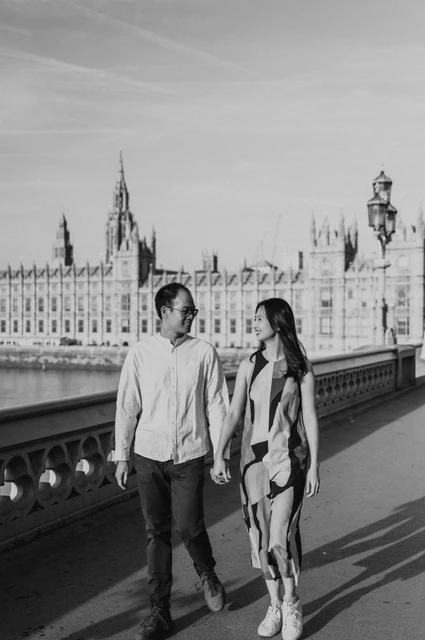Black-and-white London couple photoshoot on Westminster Bridge Black-and-white photograph of the couple walking hand in hand on Westminster Bridge with Parliament behind them, from their London couple photoshoot.
