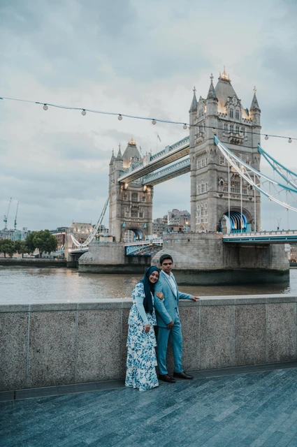 London engagement photoshoot: a portrait beside the Queen’s Walk wall An engaged couple beside a riverside wall with Tower Bridge spanning the Thames behind them during their London engagement photoshoot.