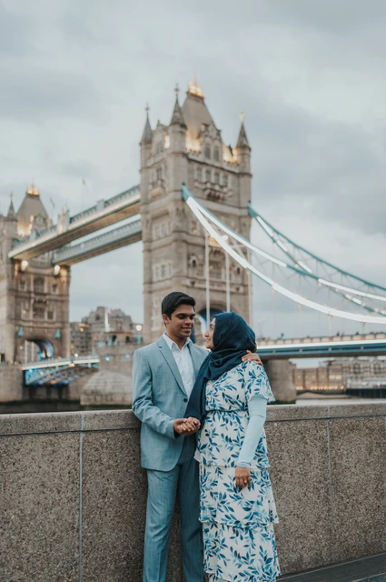 London engagement photoshoot: a quiet portrait beside the bridge A couple looking at each other beside the riverside wall with Tower Bridge above them during their London engagement photoshoot.