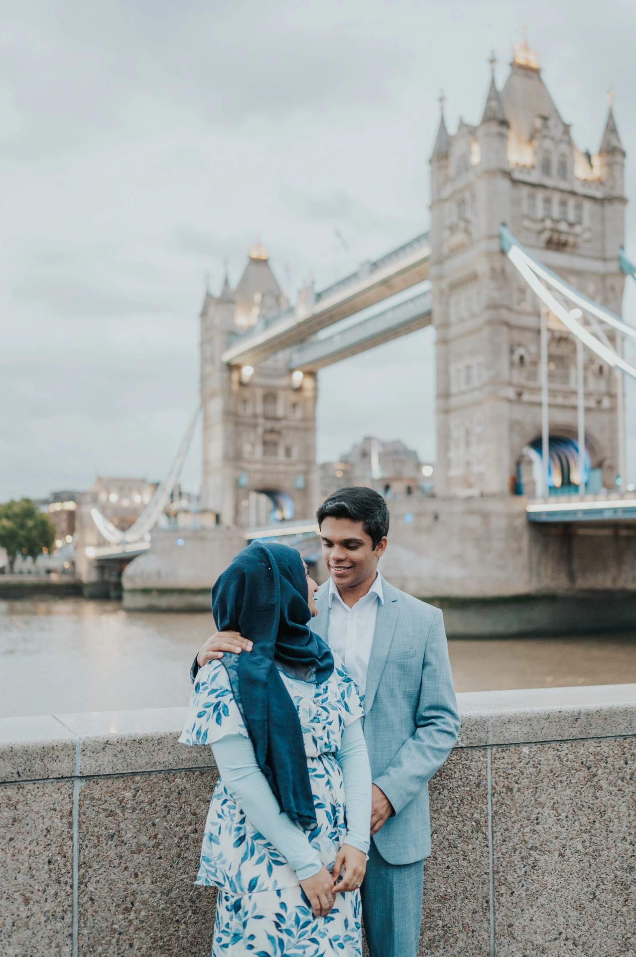 A man smiling at his partner beside the Queen’s Walk wall with Tower Bridge in the background during their London engagement photoshoot.