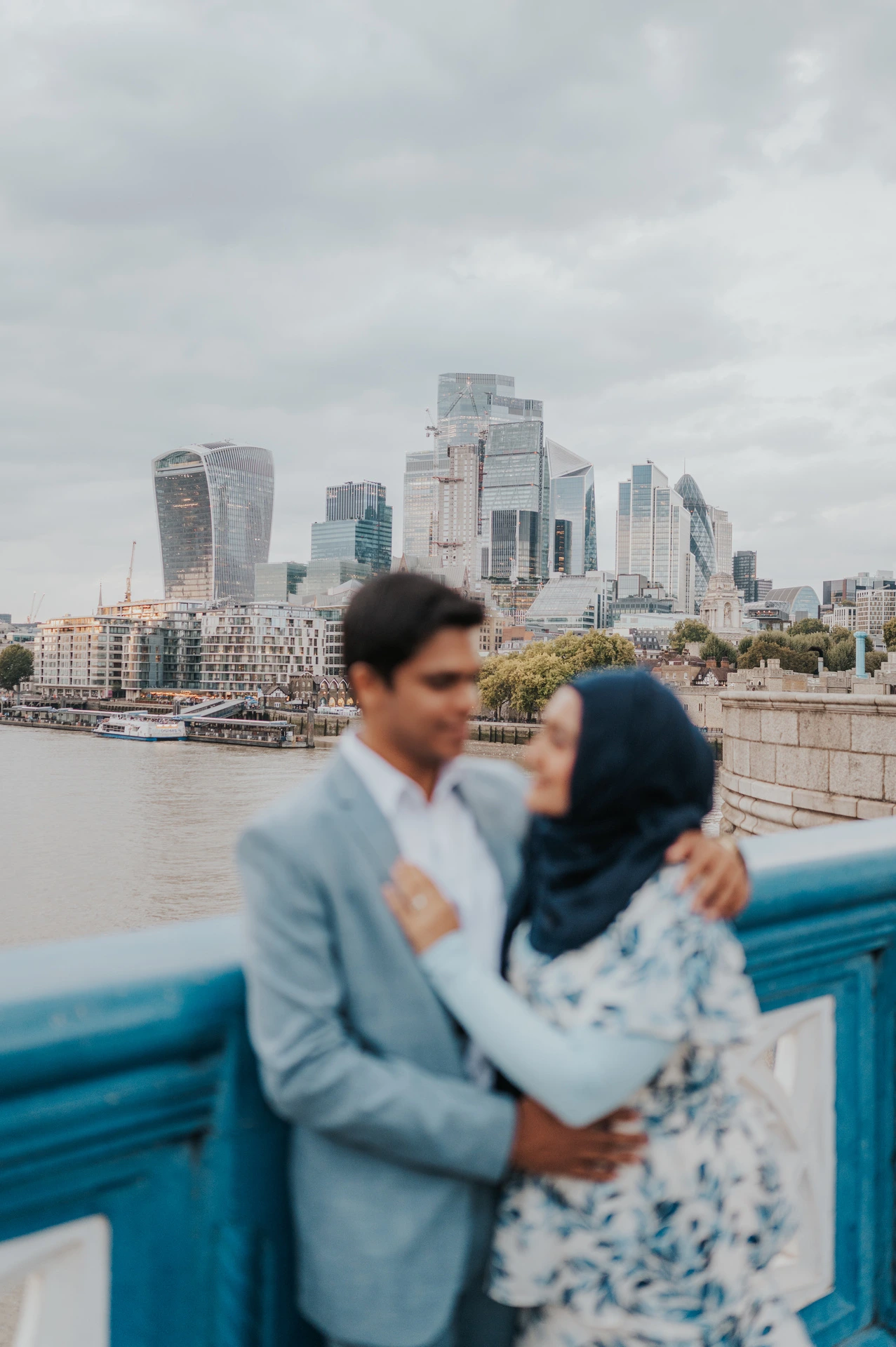 Soft-focus portrait of a couple leaning close above Tower Bridge’s blue railing during their London engagement photoshoot.