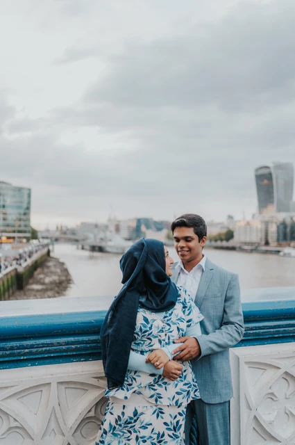 London engagement photoshoot: an embrace beside the blue bridge railing A couple embracing beside Tower Bridge’s blue railing above the Thames during their London engagement photoshoot.