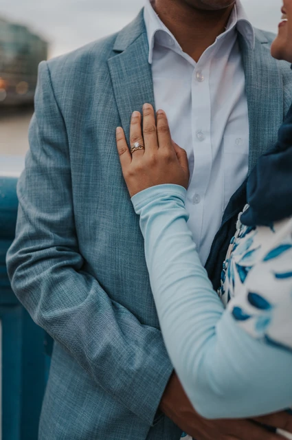 London engagement photoshoot: an engagement ring against a blue jacket A woman’s hand showing her engagement ring against her partner’s blue jacket on Tower Bridge during their London engagement photoshoot.