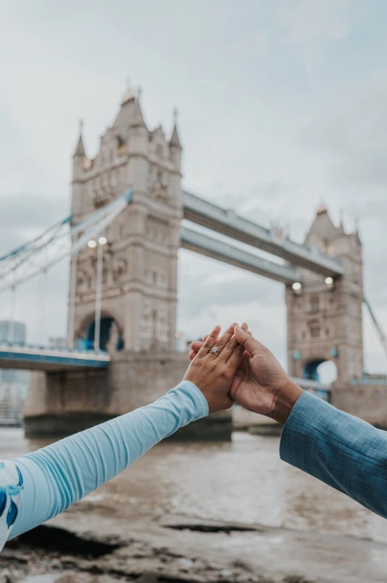 London engagement photoshoot: an engagement ring framed by Tower Bridge A couple raising their joined hands to show an engagement ring with Tower Bridge beyond during their London engagement photoshoot.