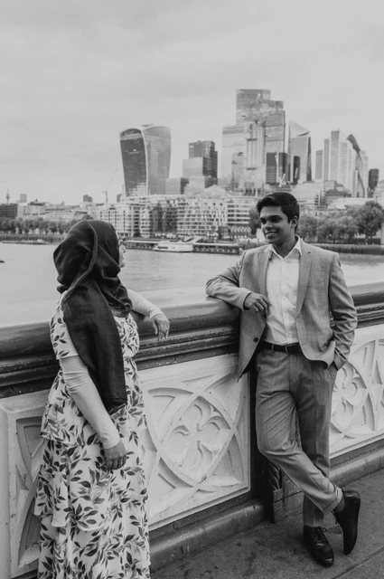 London engagement photoshoot: black-and-white portrait above the Thames Black-and-white portrait of a couple beside Tower Bridge’s railing with the City skyline behind during their London engagement photoshoot.