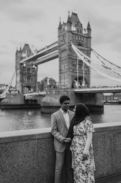 London engagement photoshoot: black-and-white portrait on the Queen’s Walk Black-and-white portrait of a couple looking at each other beside the Thames and Tower Bridge during their London engagement photoshoot.