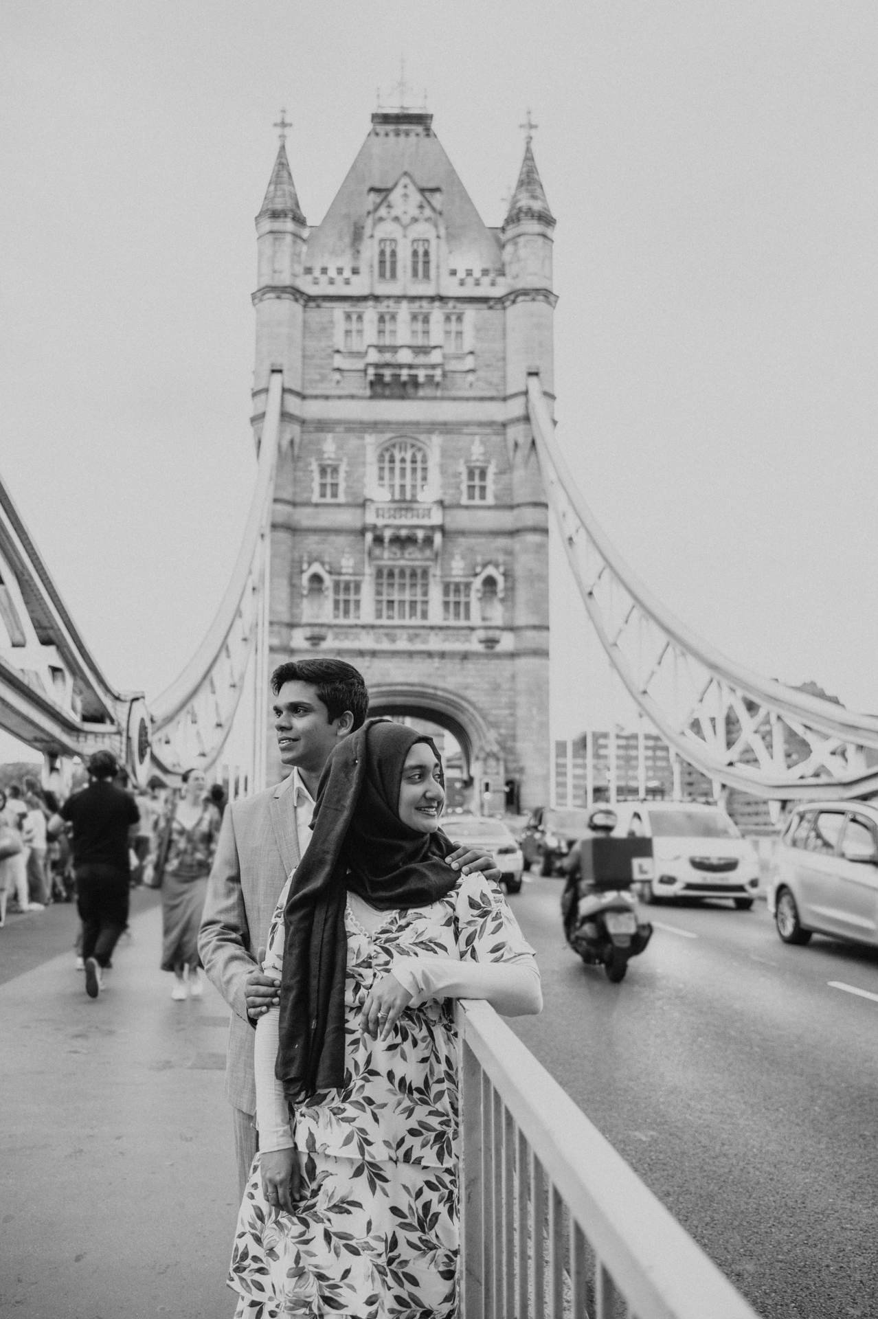 Black-and-white portrait of a couple on Tower Bridge with a stone tower rising behind them during their London engagement photoshoot.