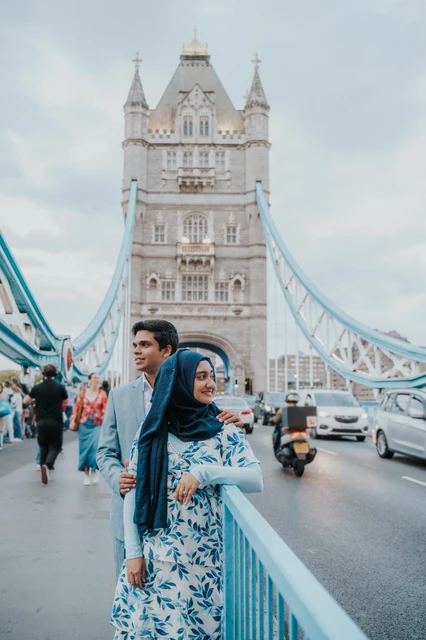 London engagement photoshoot: blue outfits on the Tower Bridge walkway A couple in blue outfits standing on Tower Bridge’s walkway with its stone tower behind them during their London engagement photoshoot.