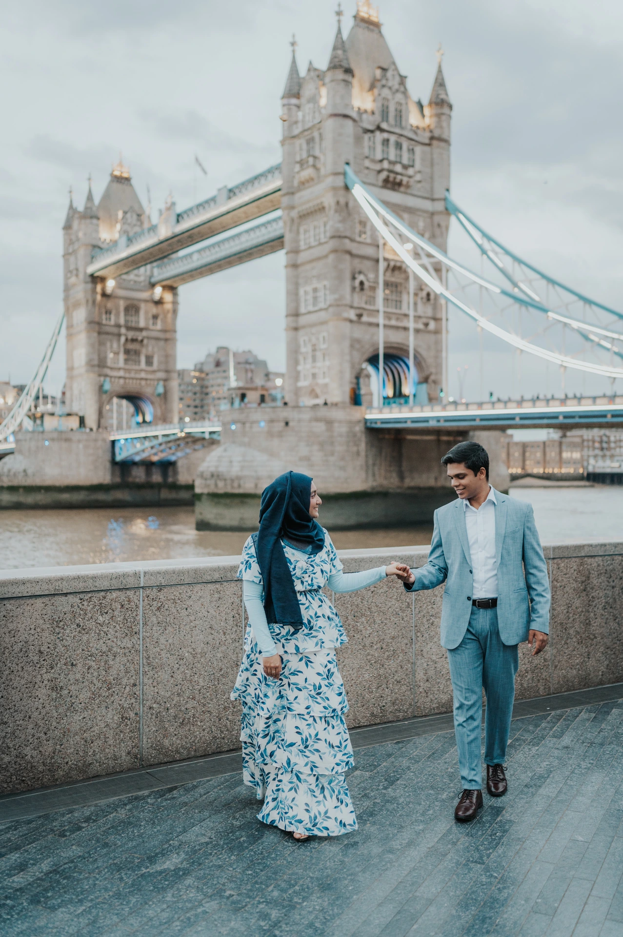 A couple holding hands while walking beside the riverside wall on the Queen’s Walk during their London engagement photoshoot.