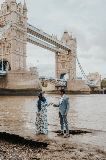 London engagement photoshoot: holding hands on the Thames foreshore A couple holding hands on the rocky foreshore with Tower Bridge in the background during their London engagement photoshoot.