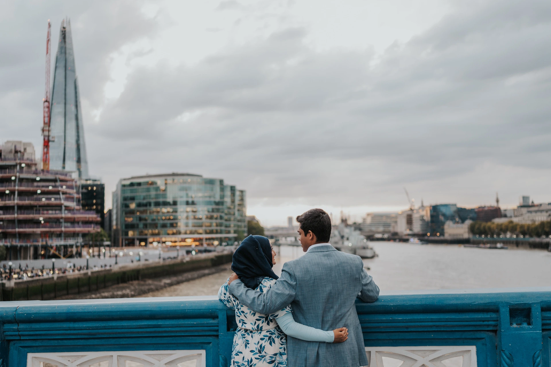A couple seen from behind looking across the Thames towards the Shard from Tower Bridge during their London engagement photoshoot.