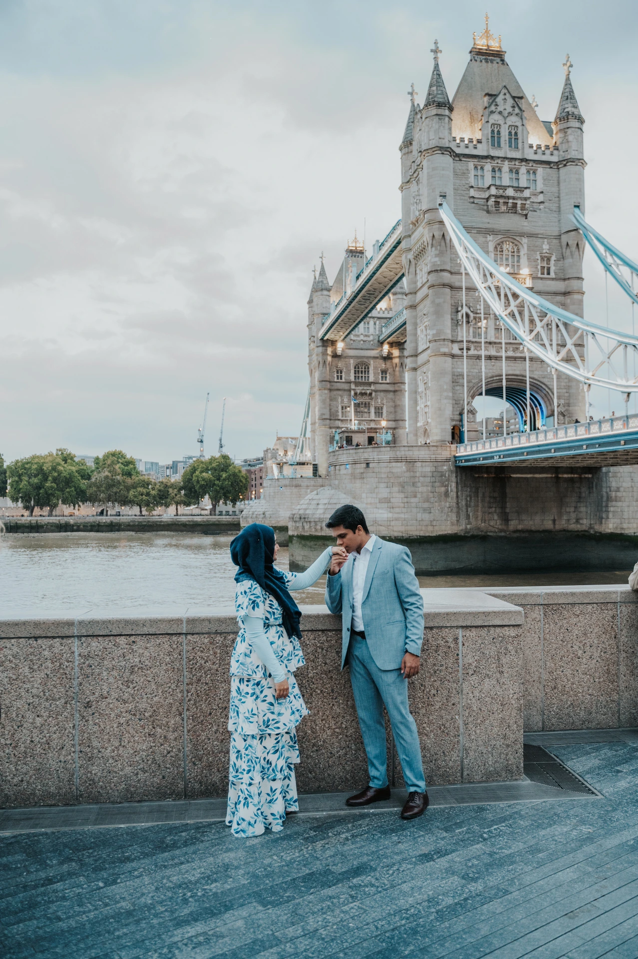 A couple standing close at the Queen’s Walk riverside wall with Tower Bridge behind them during their London engagement photoshoot.