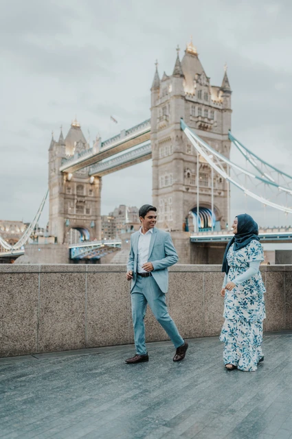 London engagement photoshoot: walking beside the Thames wall A couple walking together beside the Queen’s Walk riverside wall below Tower Bridge during their London engagement photoshoot.