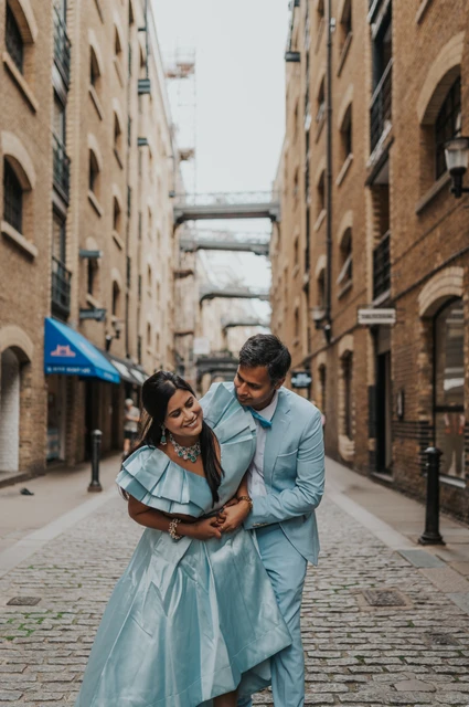 London family photoshoot: a blue-clad couple in a cobbled brick lane A couple in pale blue outfits embracing in a cobbled lane between brick warehouse buildings during their London family photoshoot.