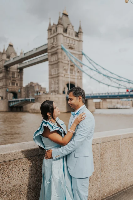 London family photoshoot: a couple portrait beside the riverside wall A couple embracing beside the riverside wall with Tower Bridge behind them during their London family photoshoot.