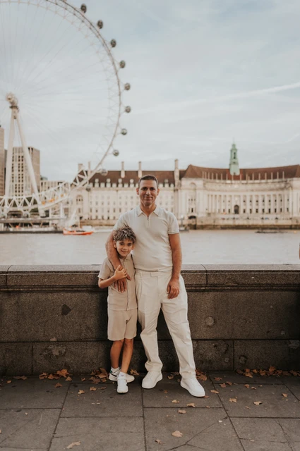 London family photoshoot: a father and child by the London Eye A father standing with a child beside the Thames with the London Eye behind them during their London family photoshoot.
