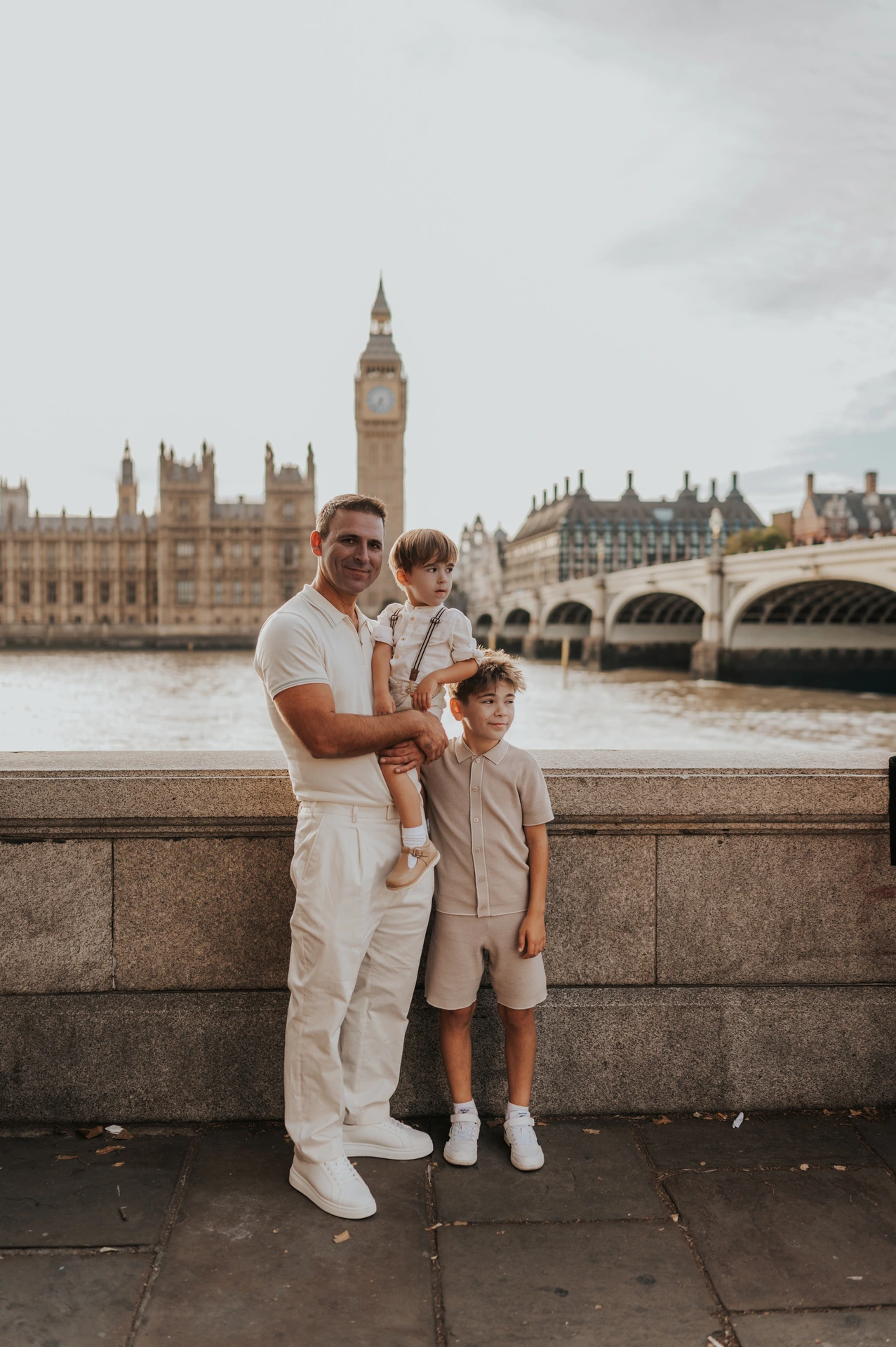A father holding his youngest child with an older child beside him and Big Ben in the background during their London family photoshoot.