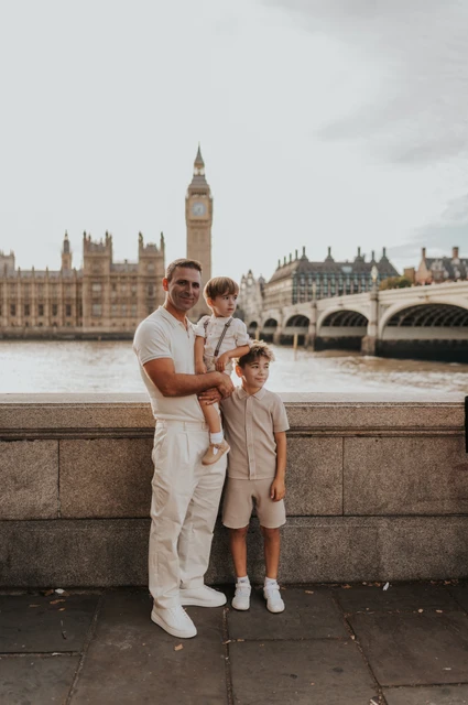 London family photoshoot: a father and children beside Big Ben A father holding his youngest child with an older child beside him and Big Ben in the background during their London family photoshoot.