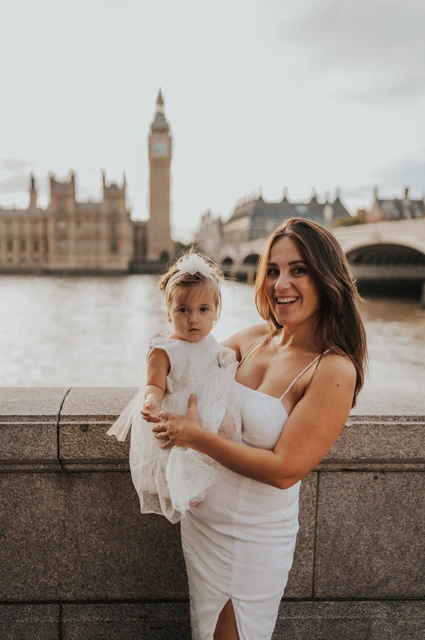 London family photoshoot: a mother and child by the Thames A smiling mother holding her young child with Big Ben softly blurred behind them during their London family photoshoot.