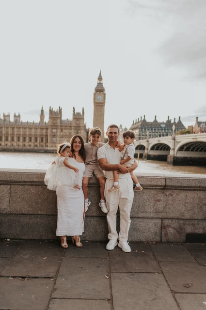 London family photoshoot: a wide family portrait with Big Ben Wide full-length portrait of a family of five beside the Thames and Big Ben during their London family photoshoot.