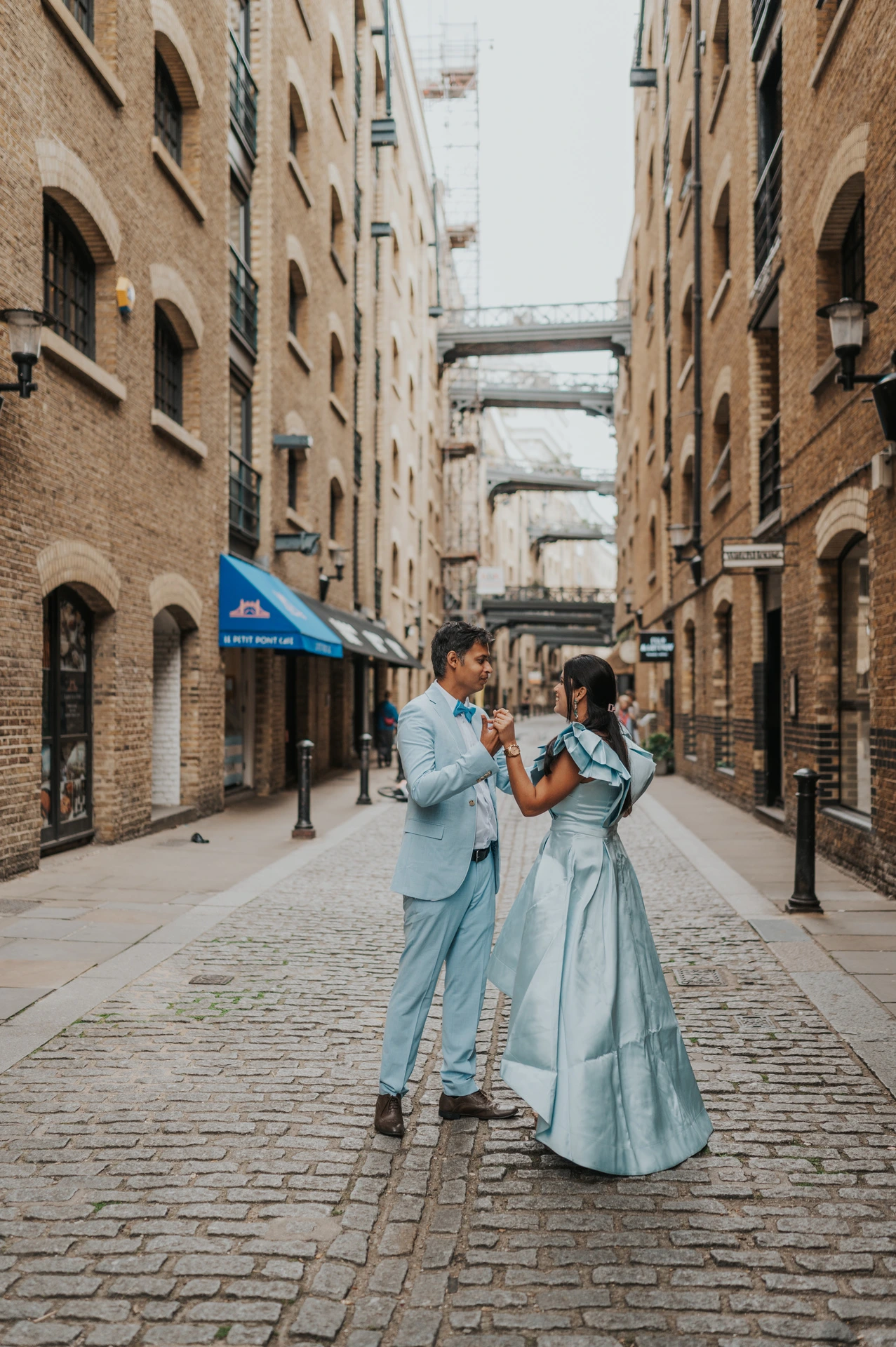 A couple embracing in the middle of a cobbled lane between brick warehouse buildings during their London family photoshoot.