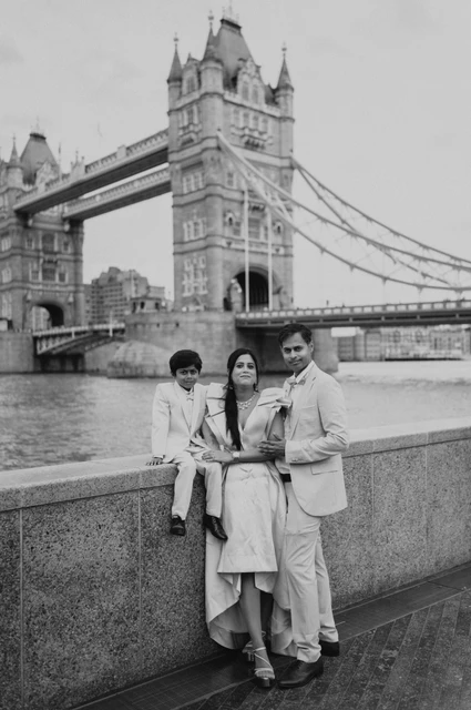 London family photoshoot: black-and-white family portrait by the Thames Black-and-white portrait of a family of three beside a riverside wall with Tower Bridge in view during their London family photoshoot.