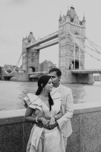 London family photoshoot: black-and-white portrait at the riverside wall Black-and-white portrait of a couple standing together beside the riverside wall with Tower Bridge behind during their London family photoshoot.