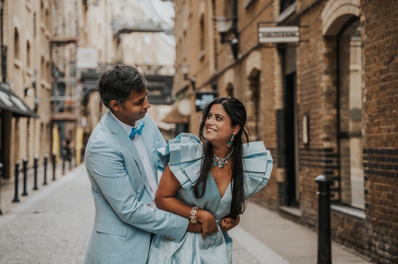 London family photoshoot: close smiles among the brick buildings A smiling couple in pale blue clothes standing close with brick buildings softly behind them during their London family photoshoot.