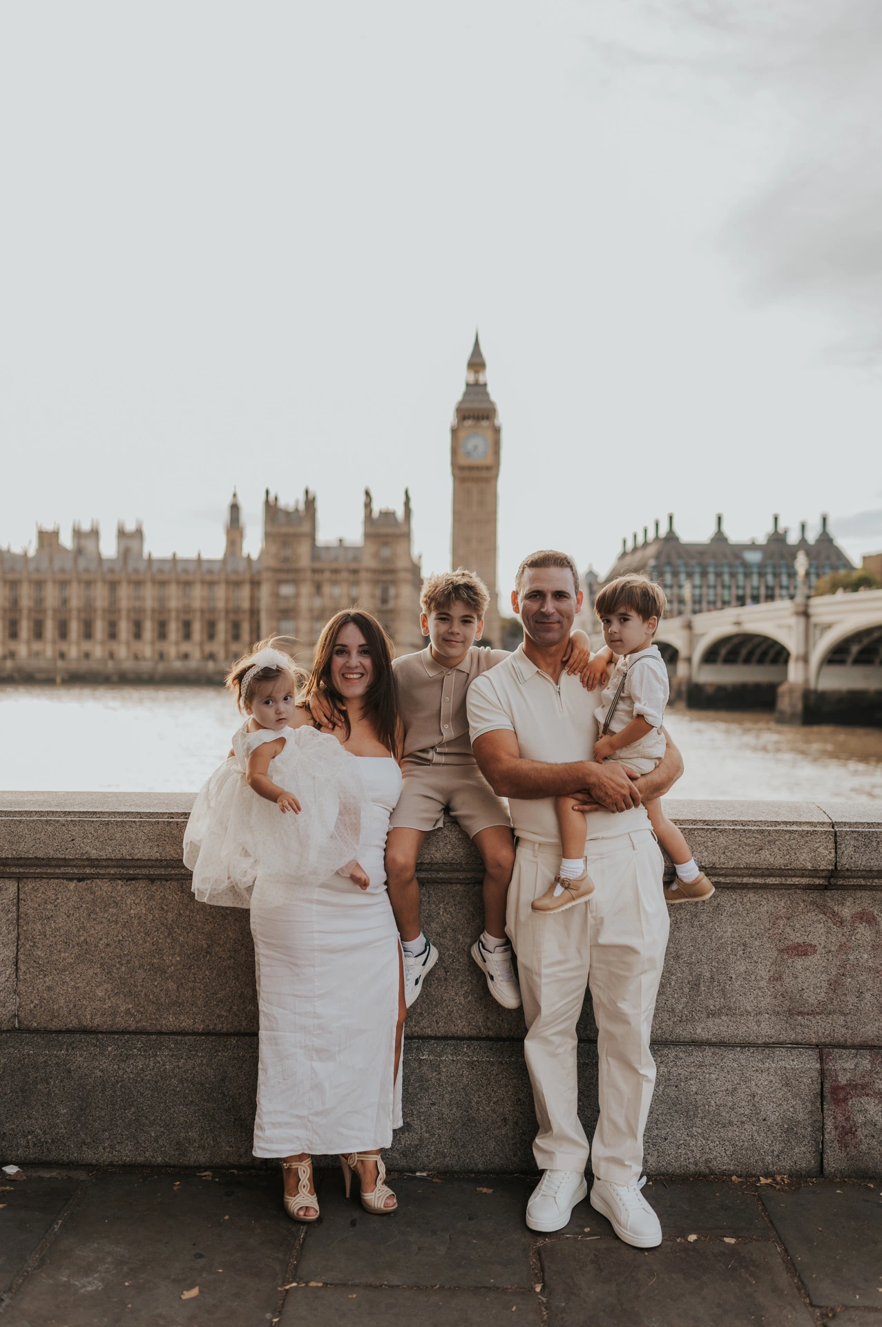 A family in cream and beige outfits beside the Thames with Big Ben rising behind them during their London family photoshoot.